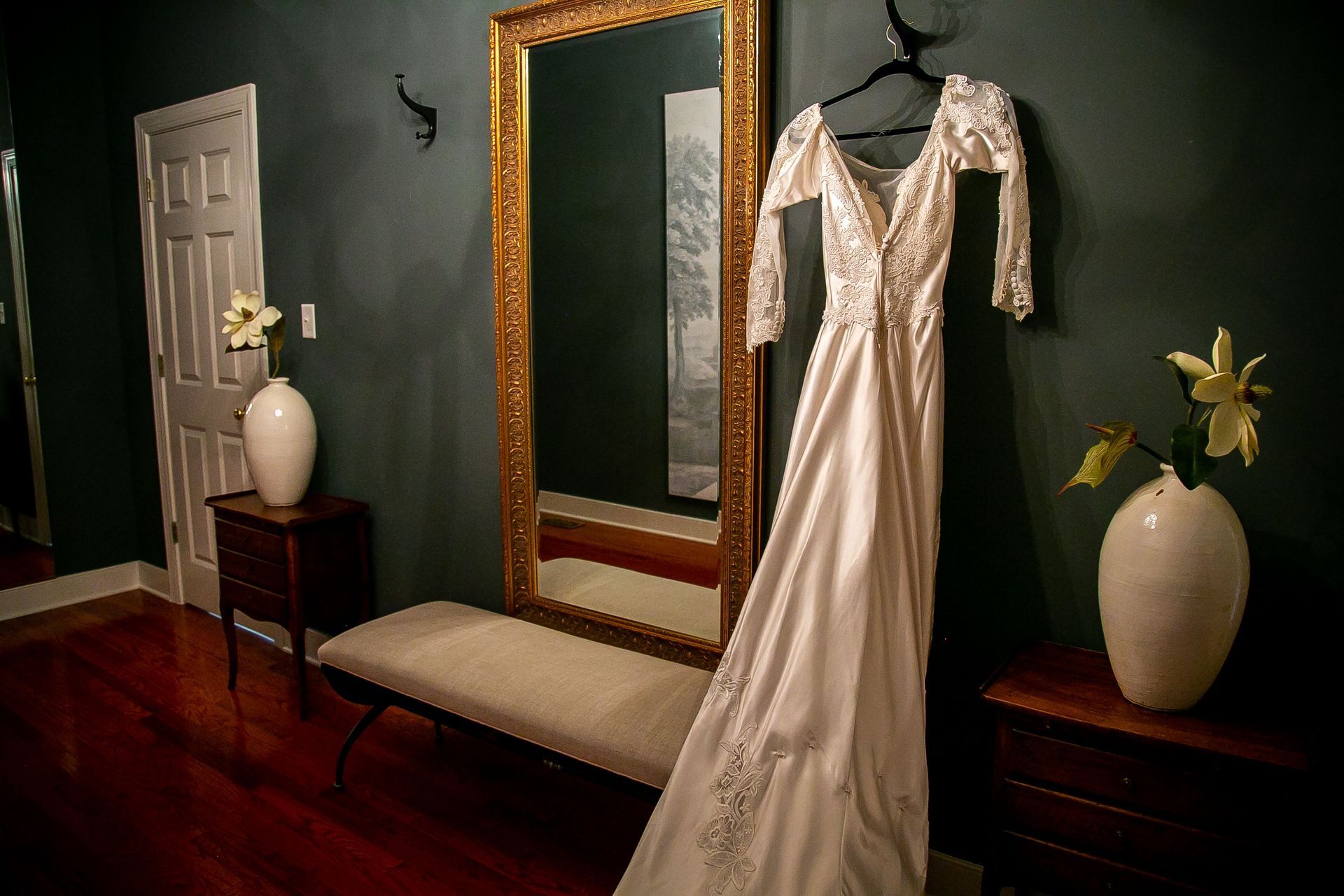 A wedding dress is hanging on a hanger in front of a mirror.