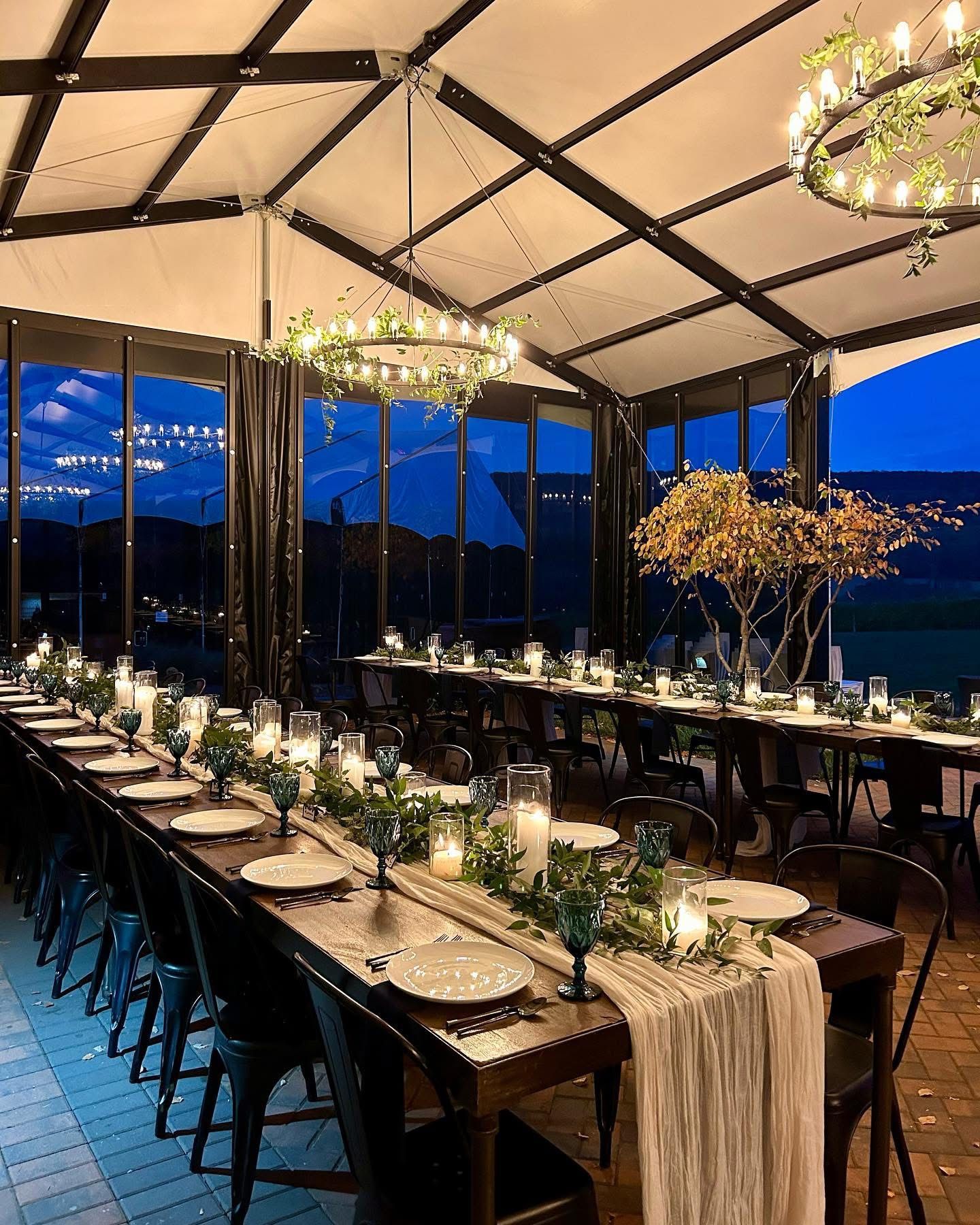 A long table with plates , glasses , candles and a chandelier.