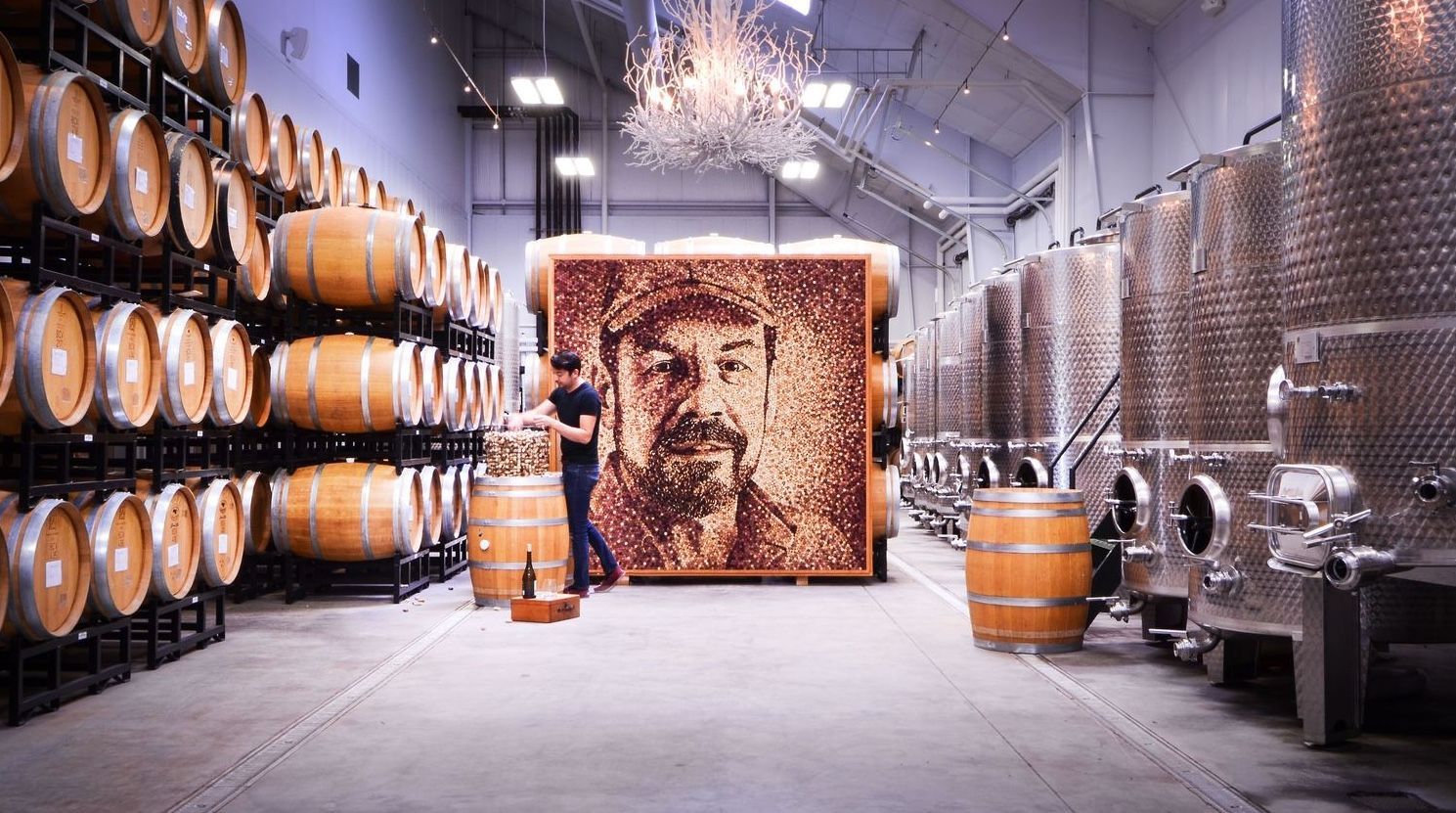 A man is standing in front of a large painting of a man in a wine cellar.