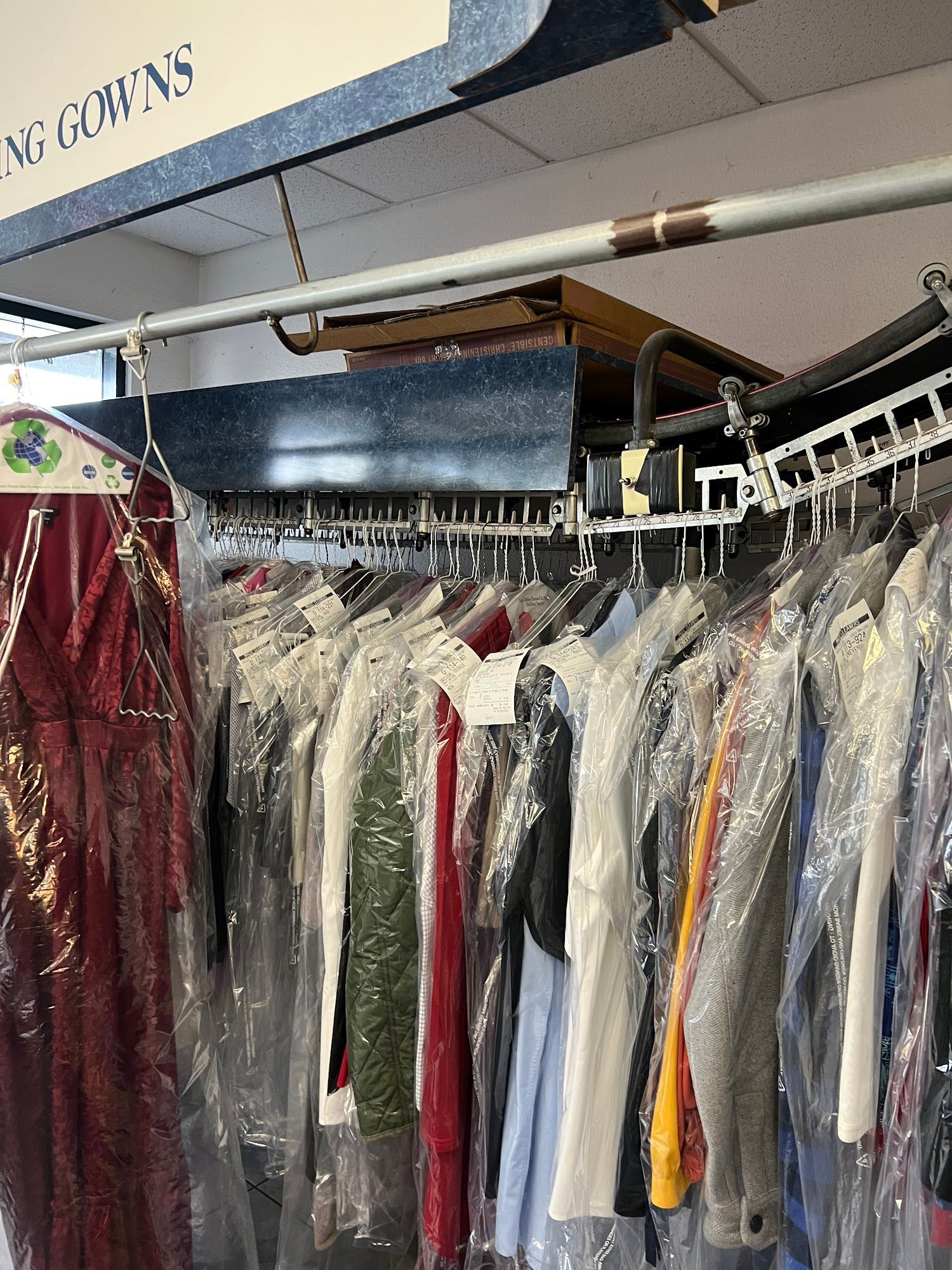 Clothes on a rack in plastic covers at a dry cleaner's, with sign above.