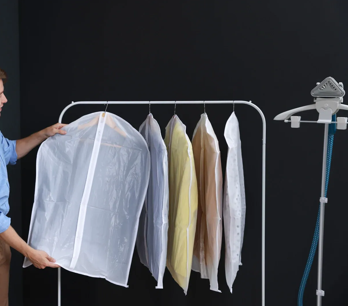 Man removing garment bag from clothes rack with shirts. Steam cleaner on the right.