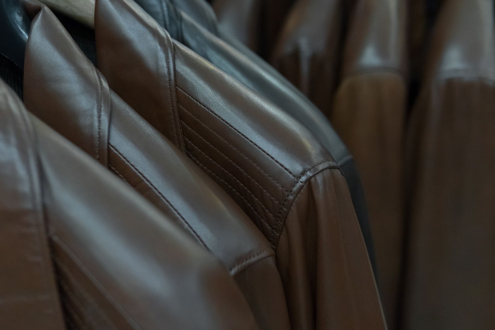 Brown leather jackets hanging on a rack, some with detailed stitching.