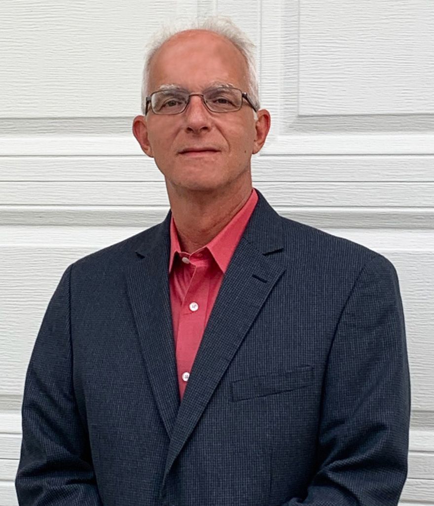 A man in a suit and red shirt is standing in front of a garage door.