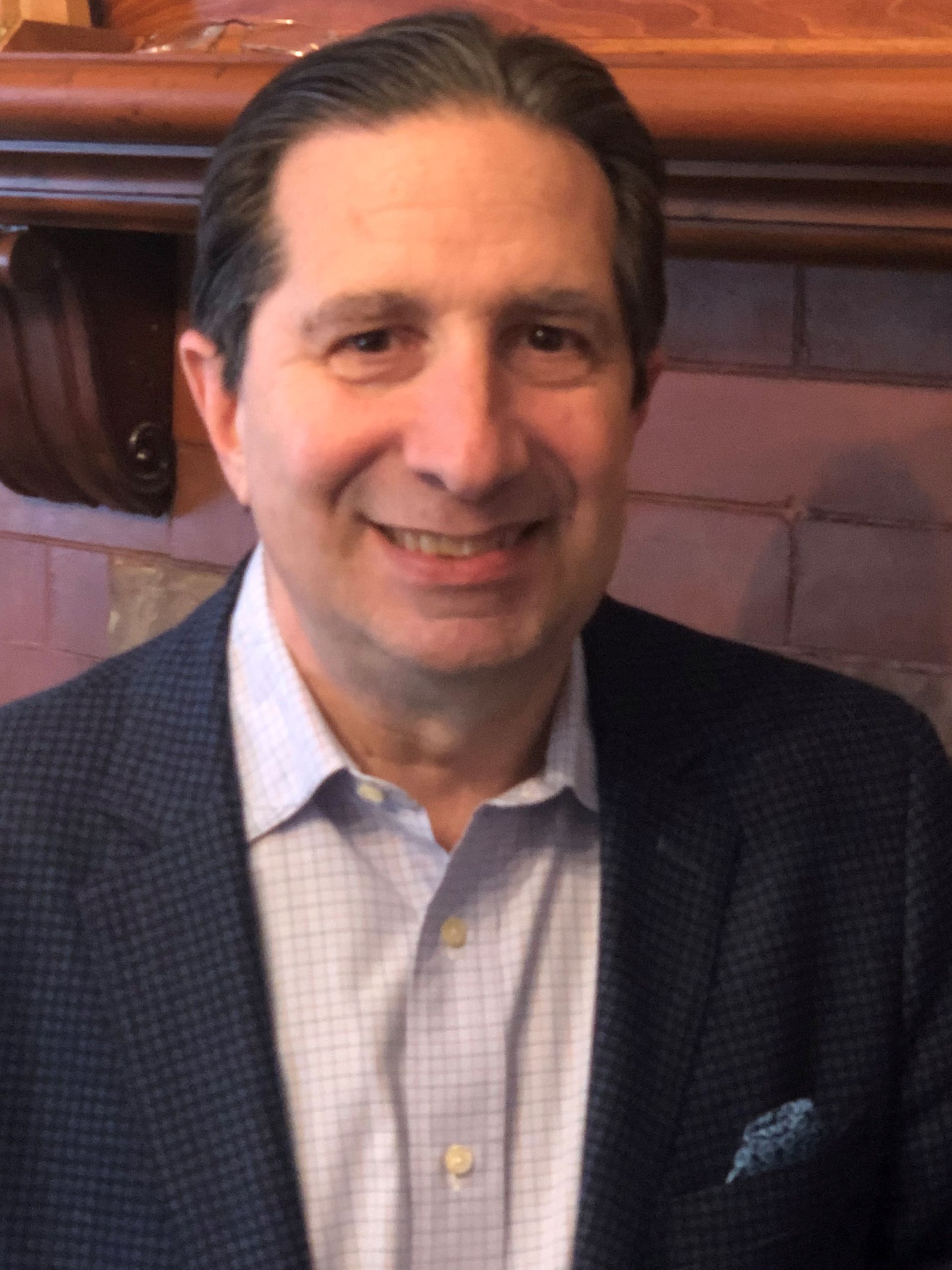A man in a suit and tie is smiling in front of a fireplace.
