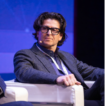 A man wearing glasses and a suit is sitting in a chair