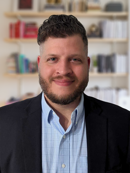 A man with a beard is wearing a suit and a blue shirt.