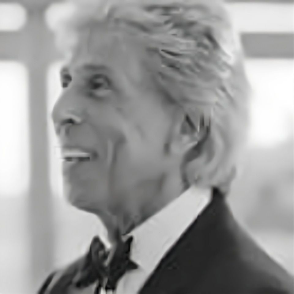 A man in a suit and bow tie is smiling in a black and white photo.