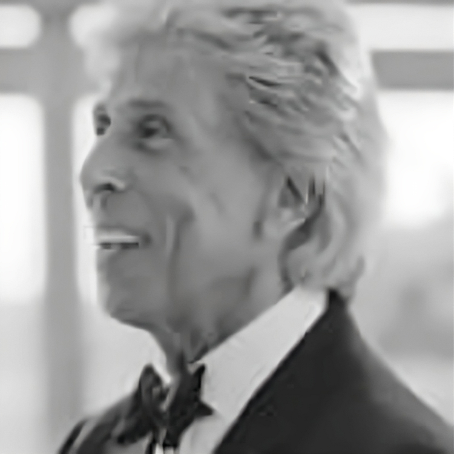 A man in a tuxedo and bow tie is smiling in a black and white photo.