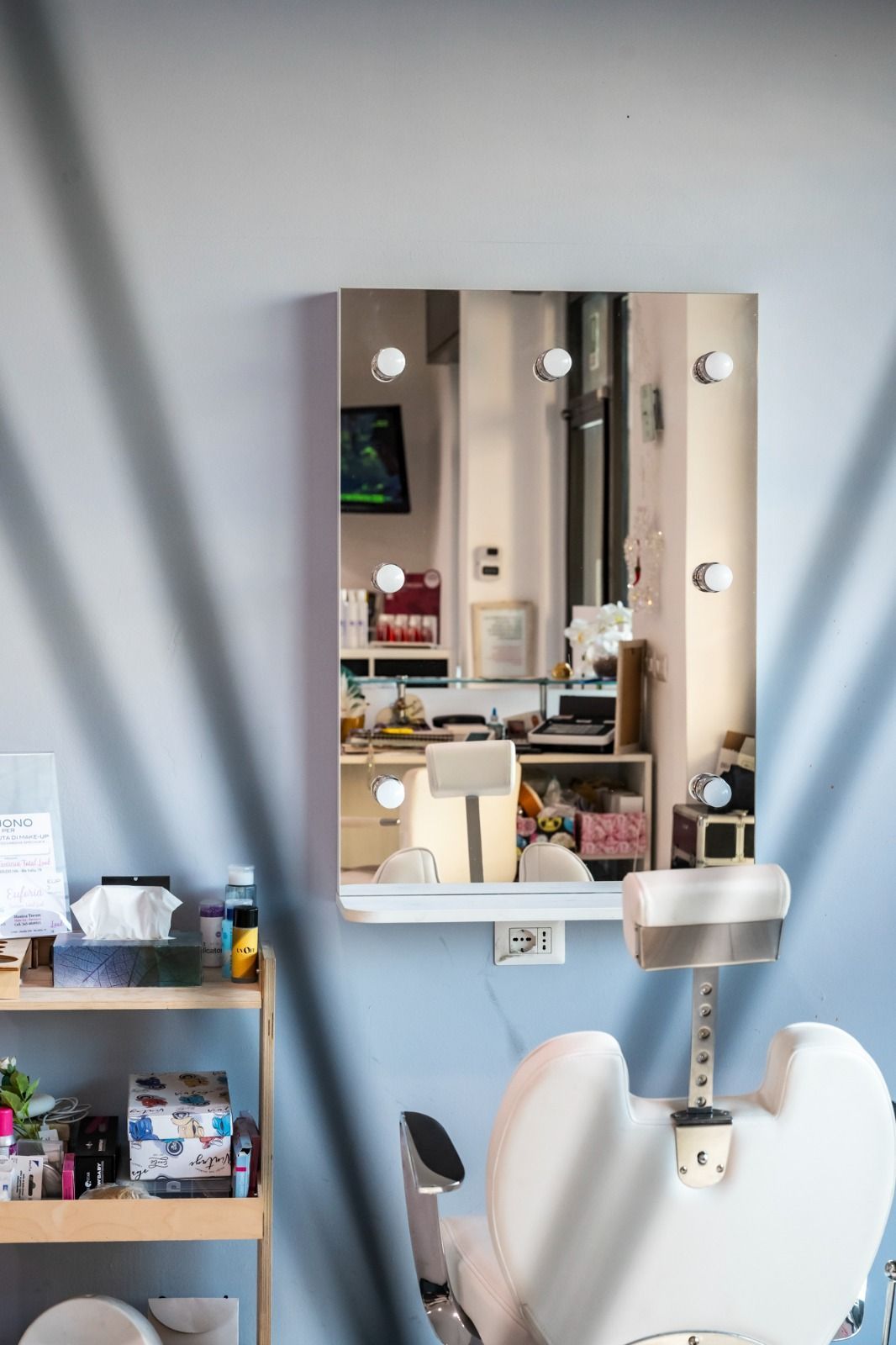 Specchio con luci in una stanza; sono visibili una sedia e degli scaffali.