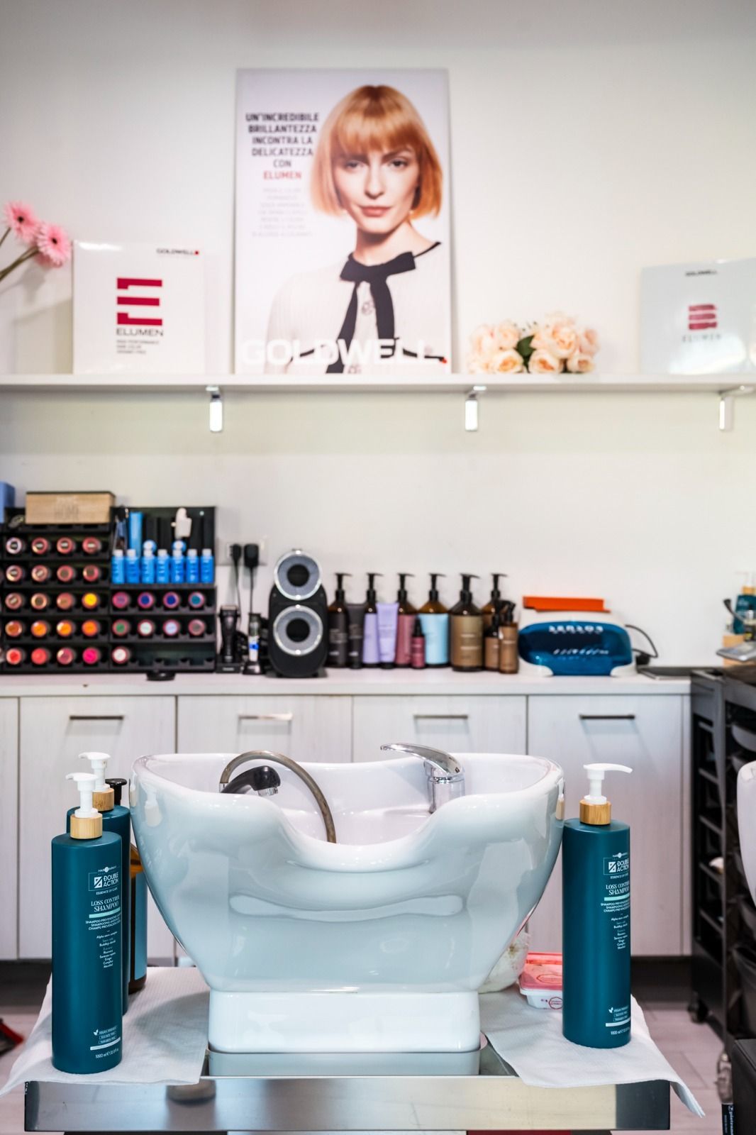 Lavandino da salone con prodotti, mensole e il ritratto di una donna con i capelli corti e arancioni.