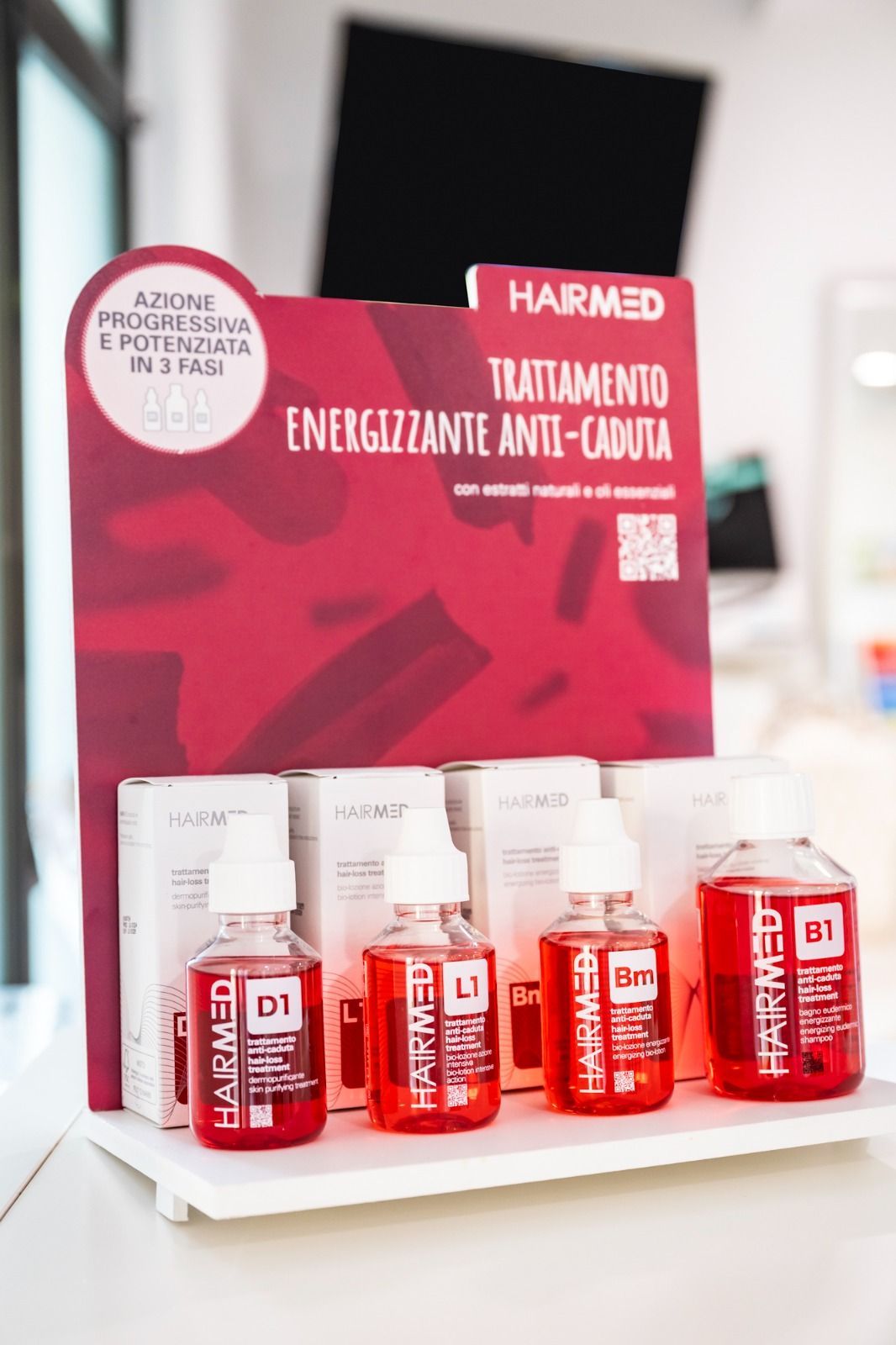 Flaconi per il trattamento della caduta dei capelli e supporto espositivo con testo, liquido rosso, confezione bianca.
