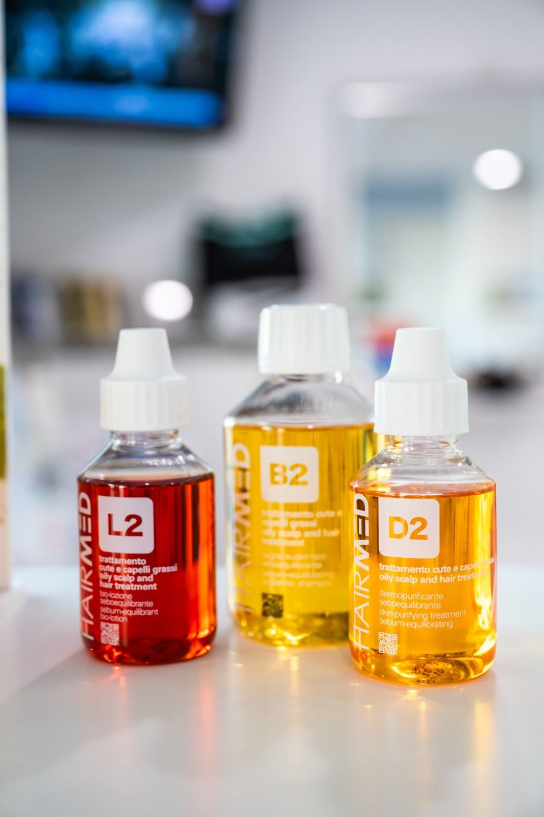 Tre bottiglie con liquidi colorati: rosso (L2), giallo (E2) e arancione (D2), su una superficie bianca.