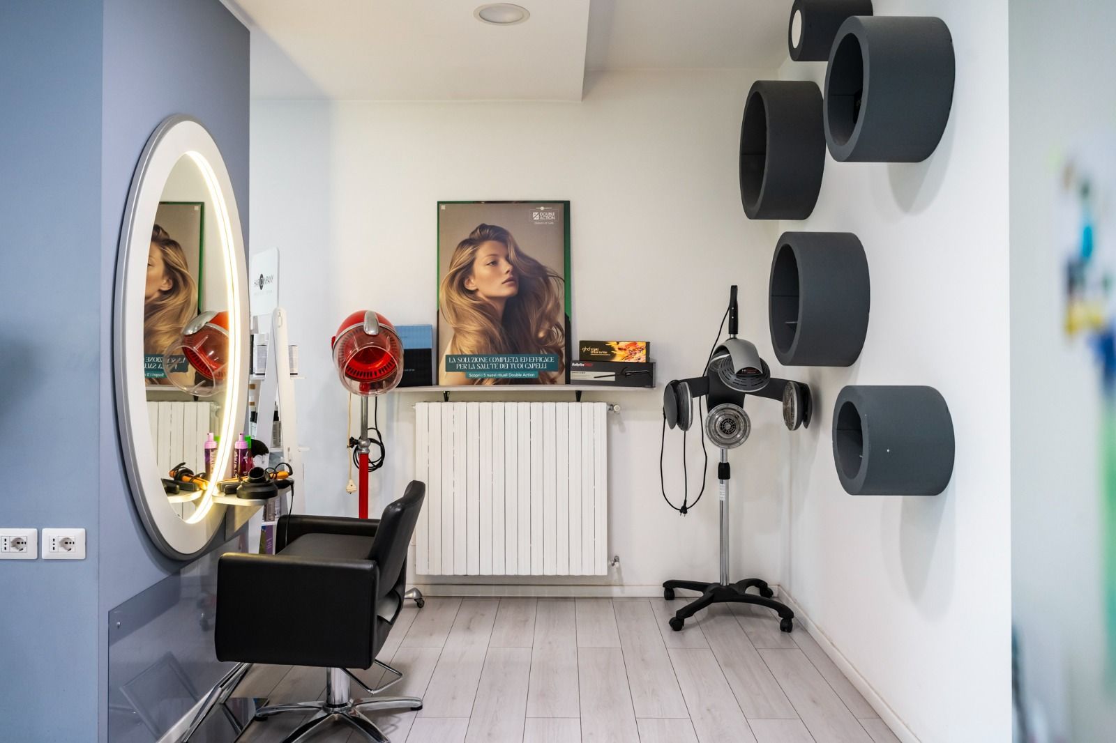 Interno di un salone da parrucchiere con sedia, specchio, asciugacapelli, poster e anelli decorativi da parete.