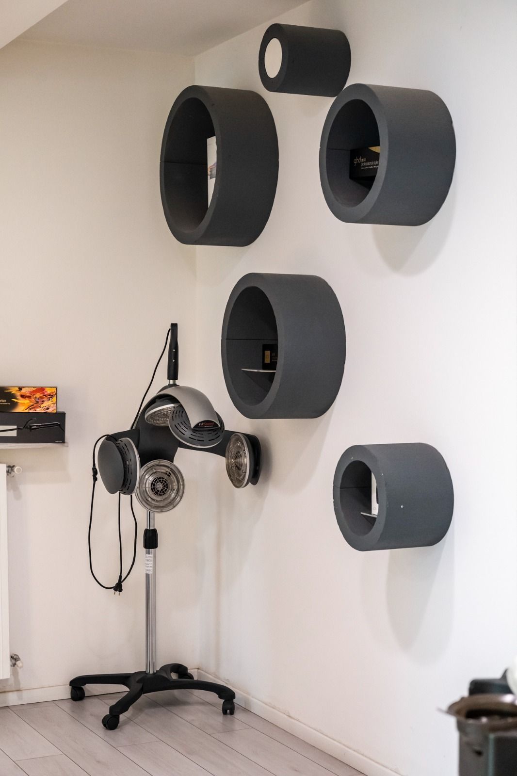 Un salone con mensole grigie circolari a parete e un asciugacapelli da terra.