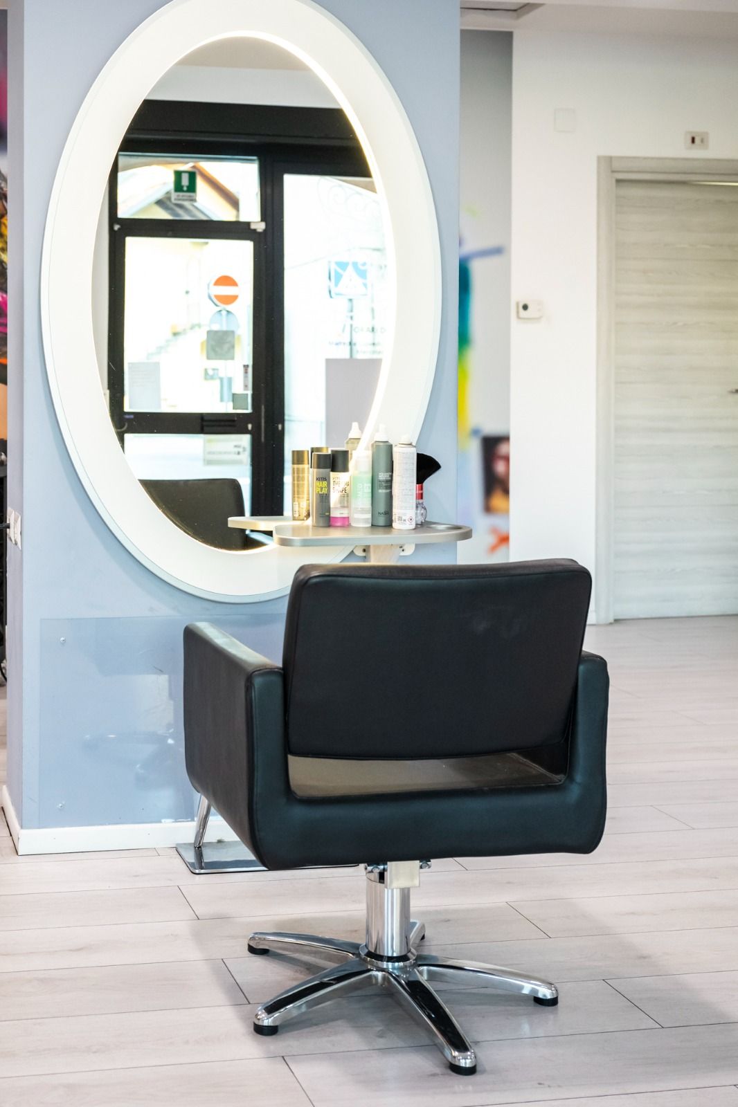 Poltrona da salone nera davanti a un grande specchio ovale.