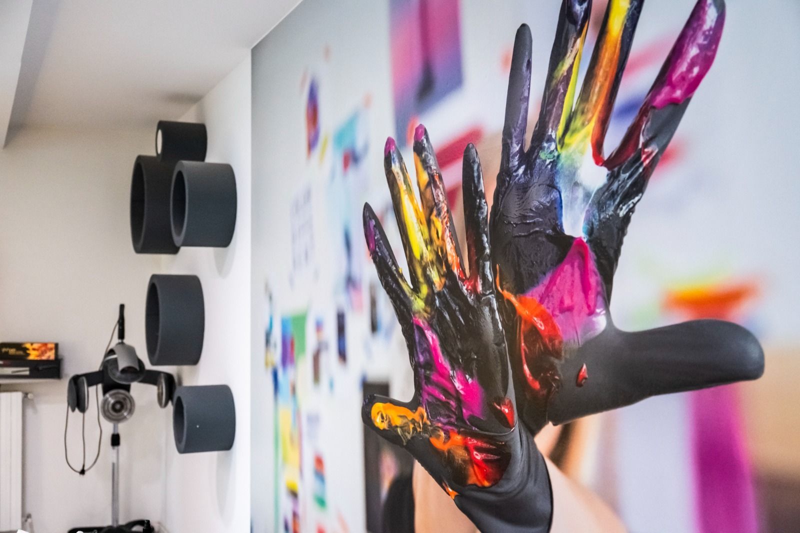 Mani ricoperte di vernice colorata, contro una parete decorata con opere d'arte.