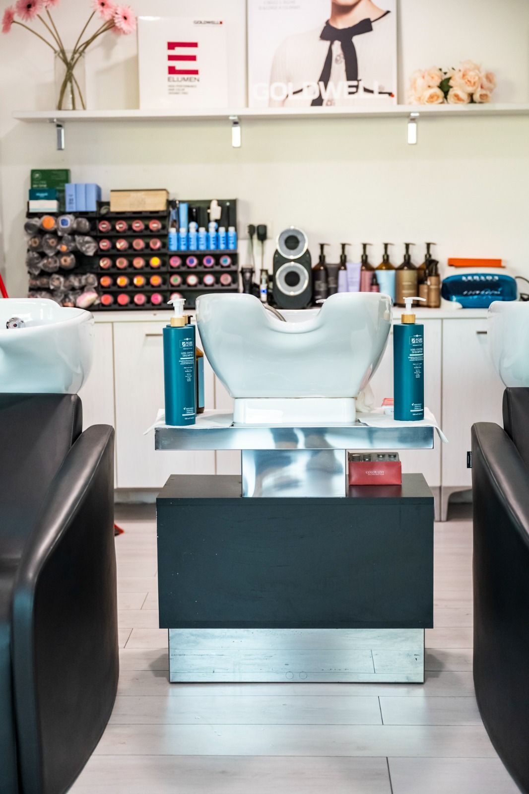 Interno di un salone da parrucchiere con postazioni per lo shampoo. Flaconi di shampoo su un bancone e scaffali con i prodotti.