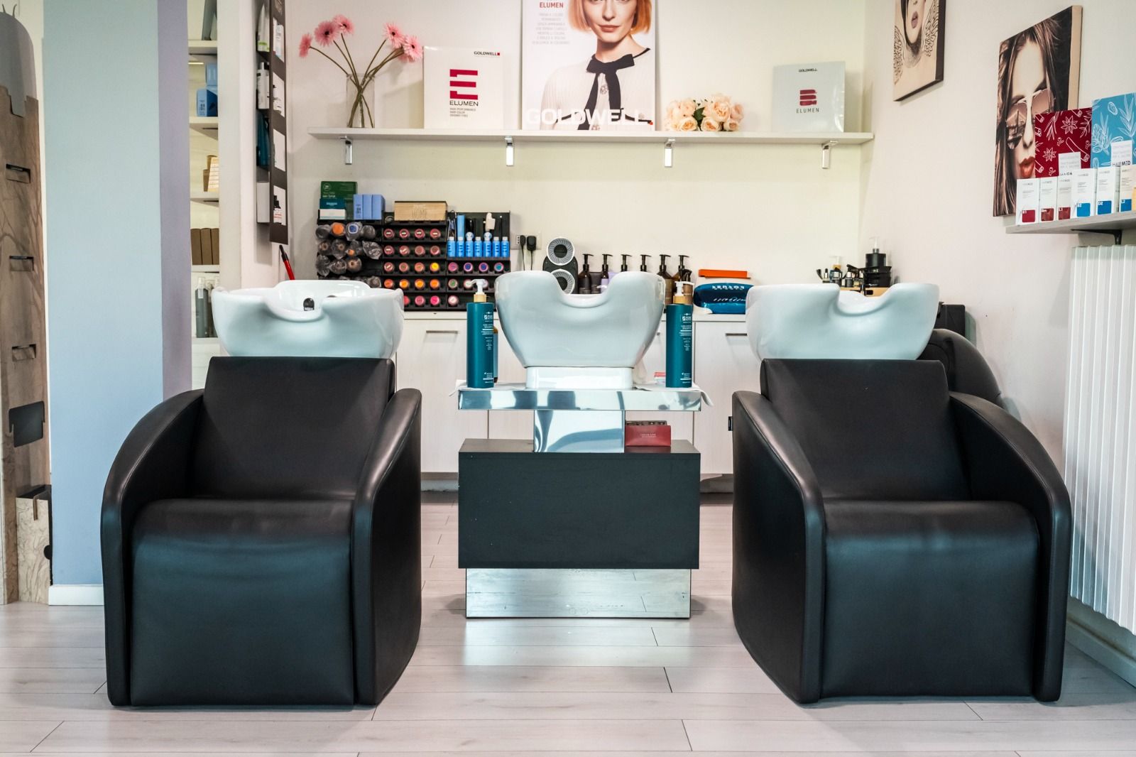 Salone con tre poltrone per lo shampoo, lavandini bianchi e poltrone in pelle nera.