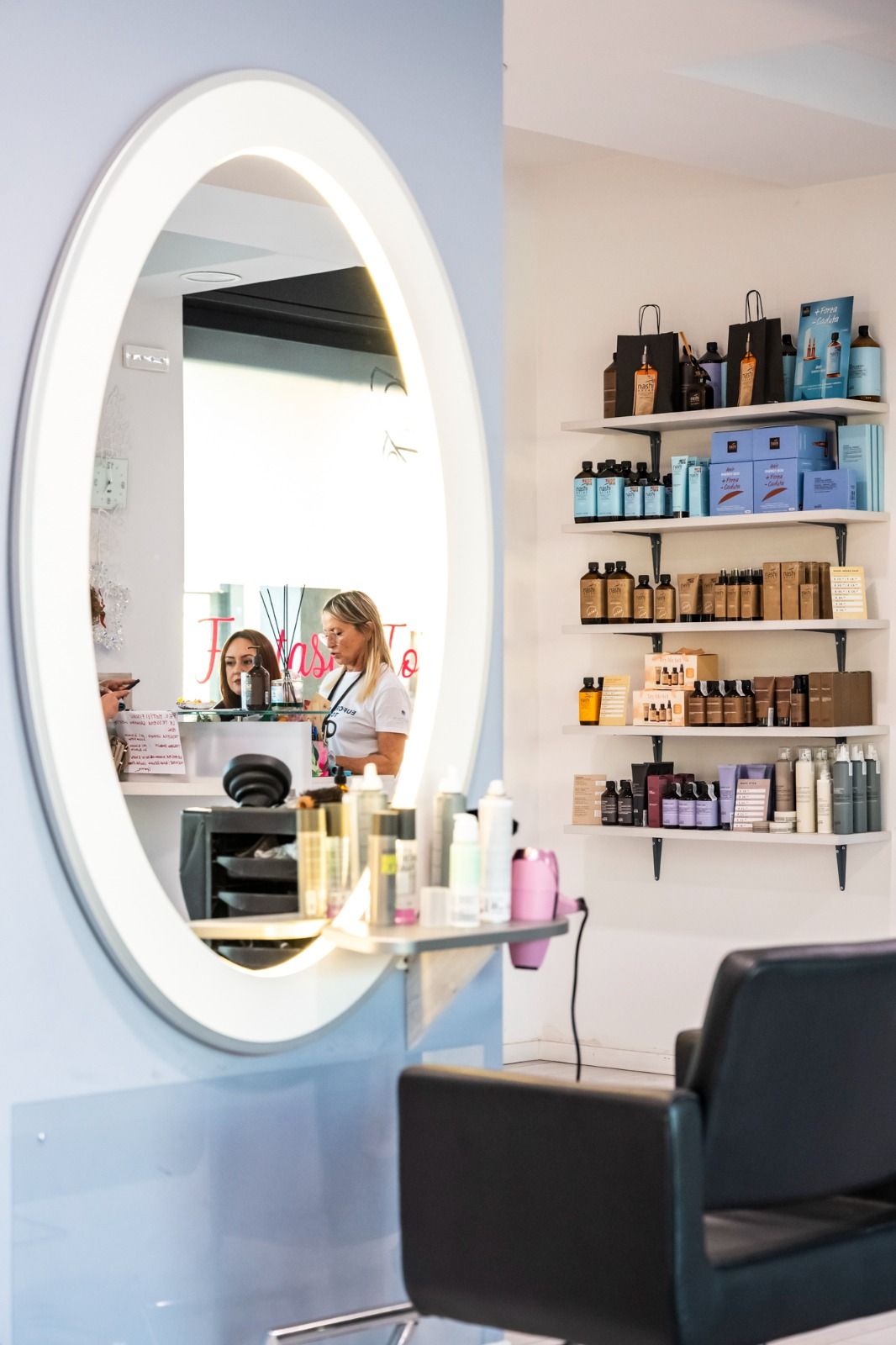 Specchio ovale in un salone da parrucchiere; parrucchiere con cliente; prodotti sugli scaffali.