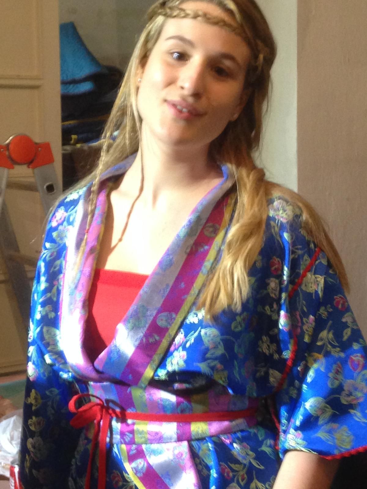 Donna in vestaglia blu con top rosso e fascia intrecciata, che guarda la telecamera.