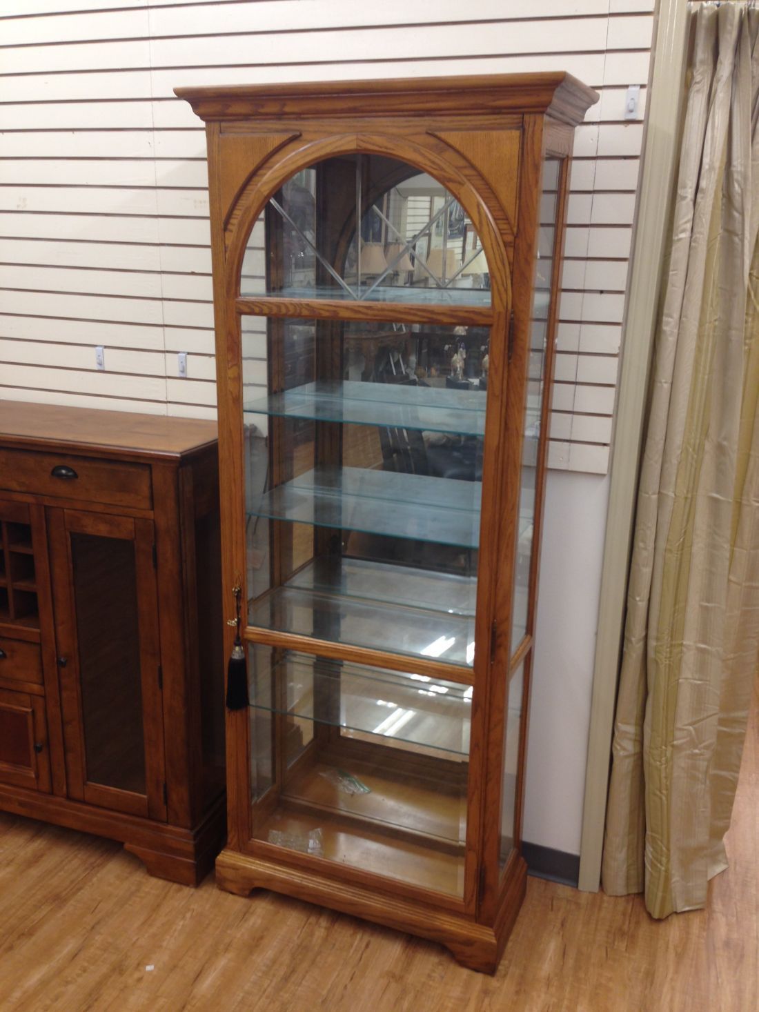 A wooden curio cabinet with glass shelves is sitting on a wooden floor.