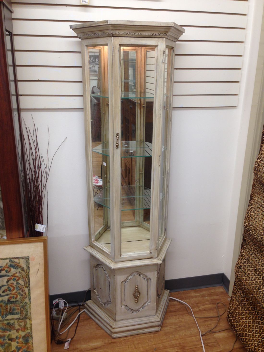 A white curio cabinet is sitting on a wooden floor in a room.