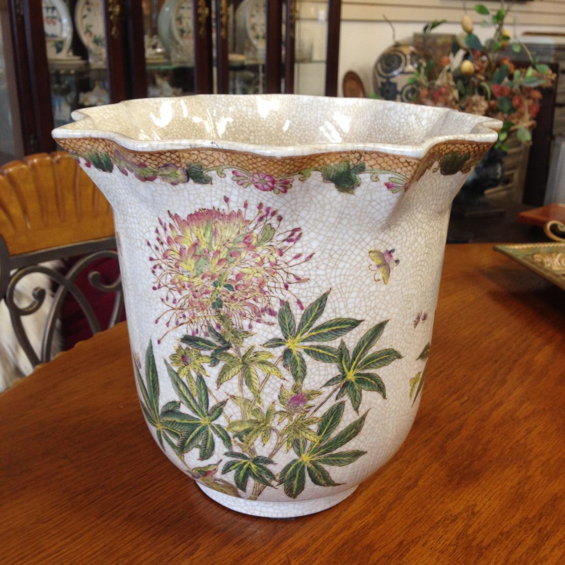 A white vase with flowers and leaves on it is sitting on a wooden table.