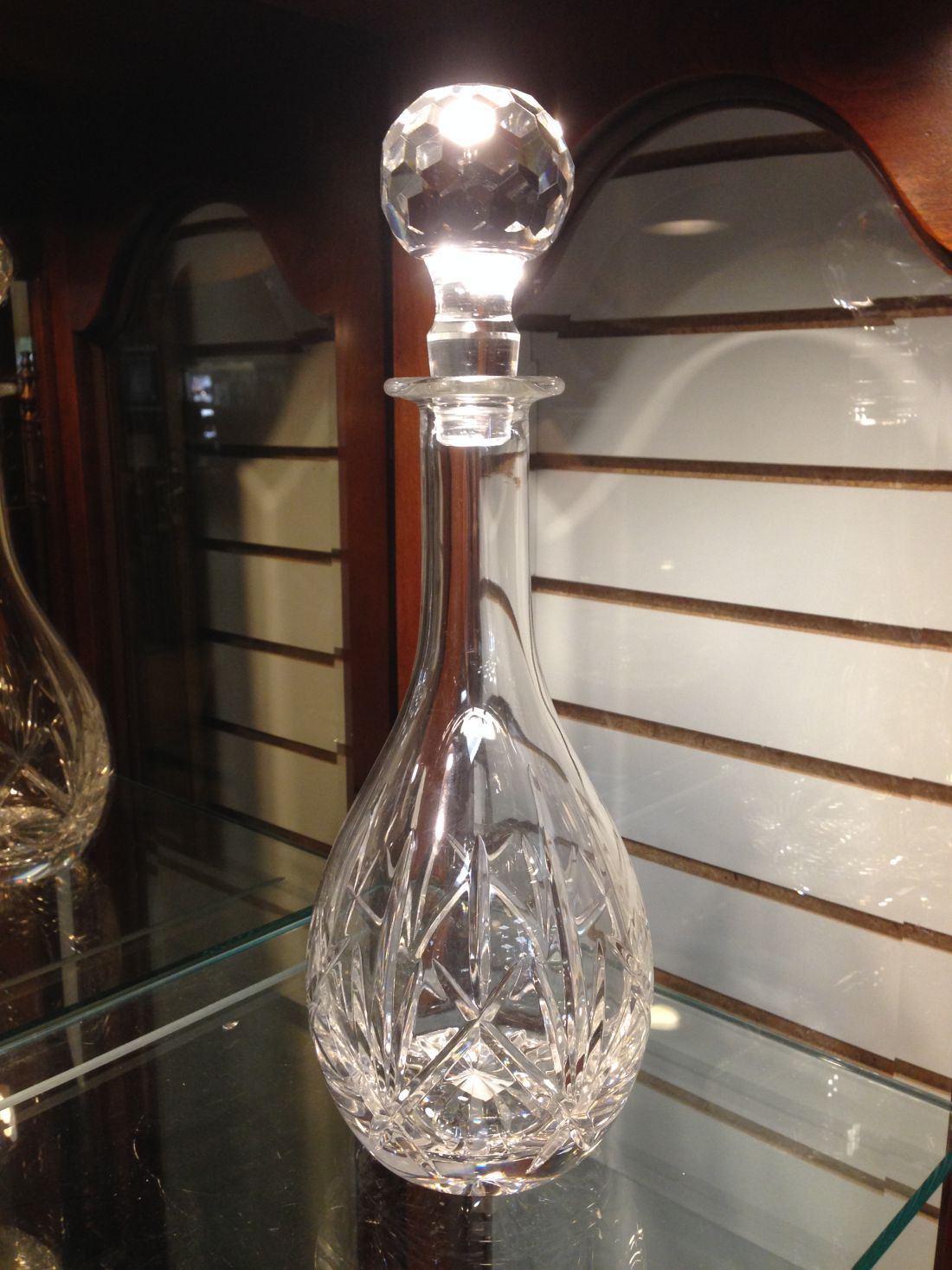 A clear glass decanter with a crystal top sits on a glass shelf