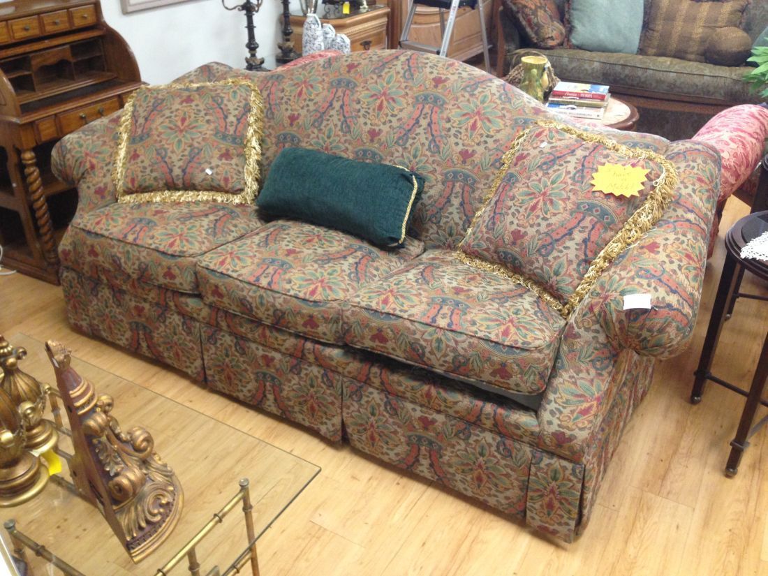 A couch with a green pillow on it is sitting on a wooden floor in a living room.