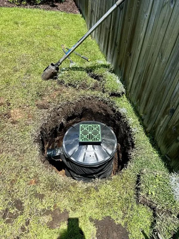 A circular drain basin in a hole dug in a grassy yard, with a shovel nearby.