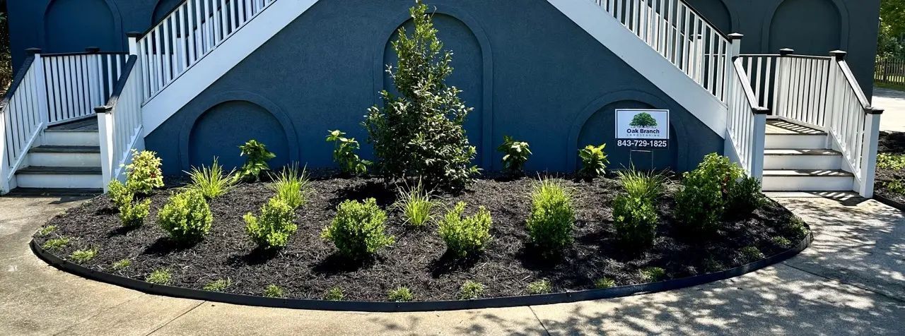 Building exterior with blue facade, white stairs, and a central garden bed of shrubs, mulch, and a small tree.