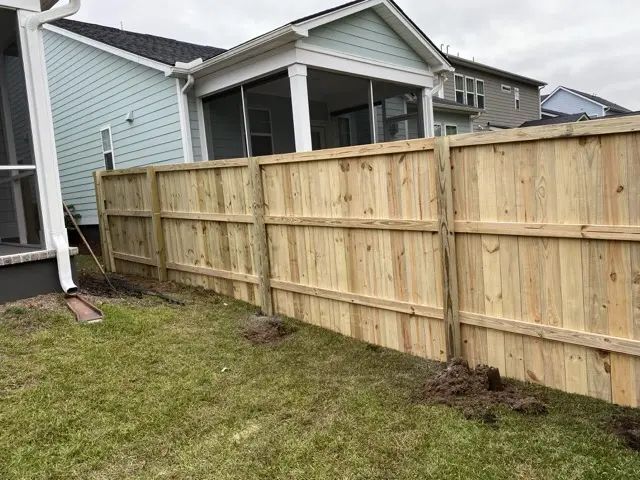 Wooden fence bordering a grassy backyard, adjacent to a house with light blue siding.
