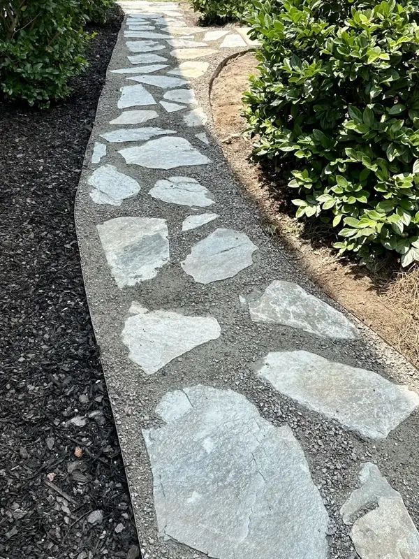 Stone pathway with irregular, gray flagstones and gravel border through a garden.