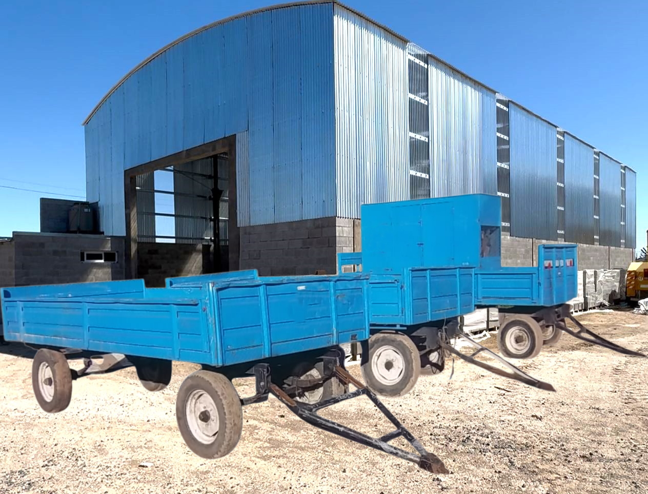 Dos carros de plataforma azules estacionados frente a un almacén de metal en un día soleado.