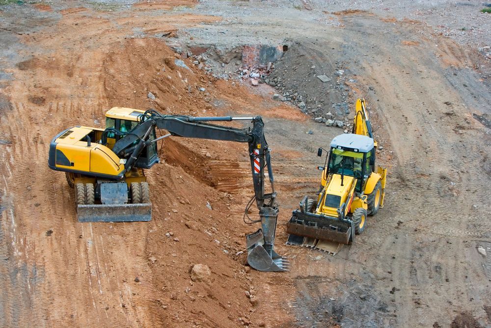 Dos vehículos de construcción amarillos excavando tierra en un sitio de construcción.