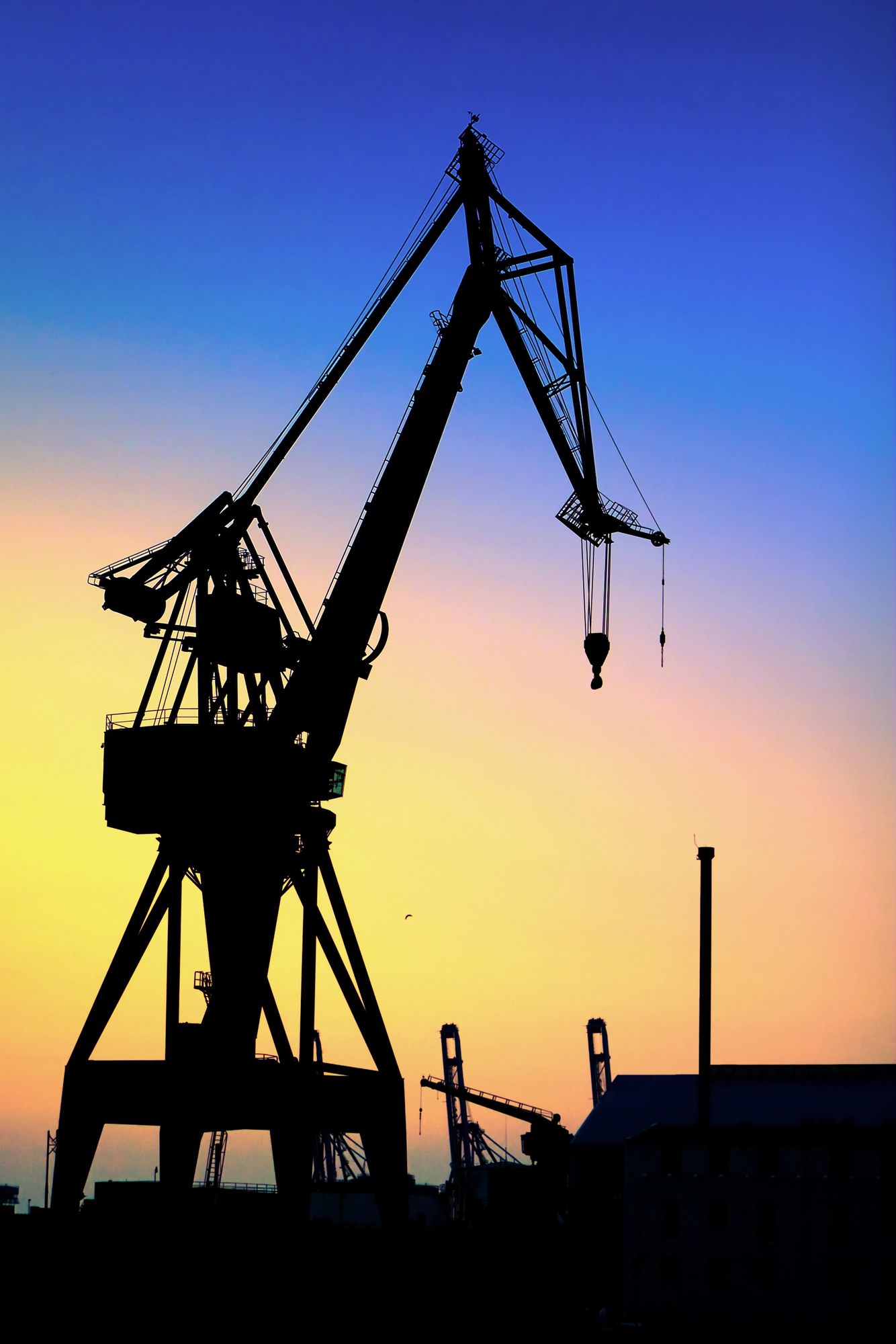 Silueta de una gran grúa contra un cielo colorido al atardecer en un puerto.
