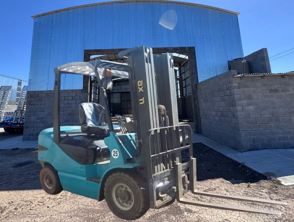 Carretilla elevadora turquesa frente a un edificio de lona azul sobre un terreno de grava.