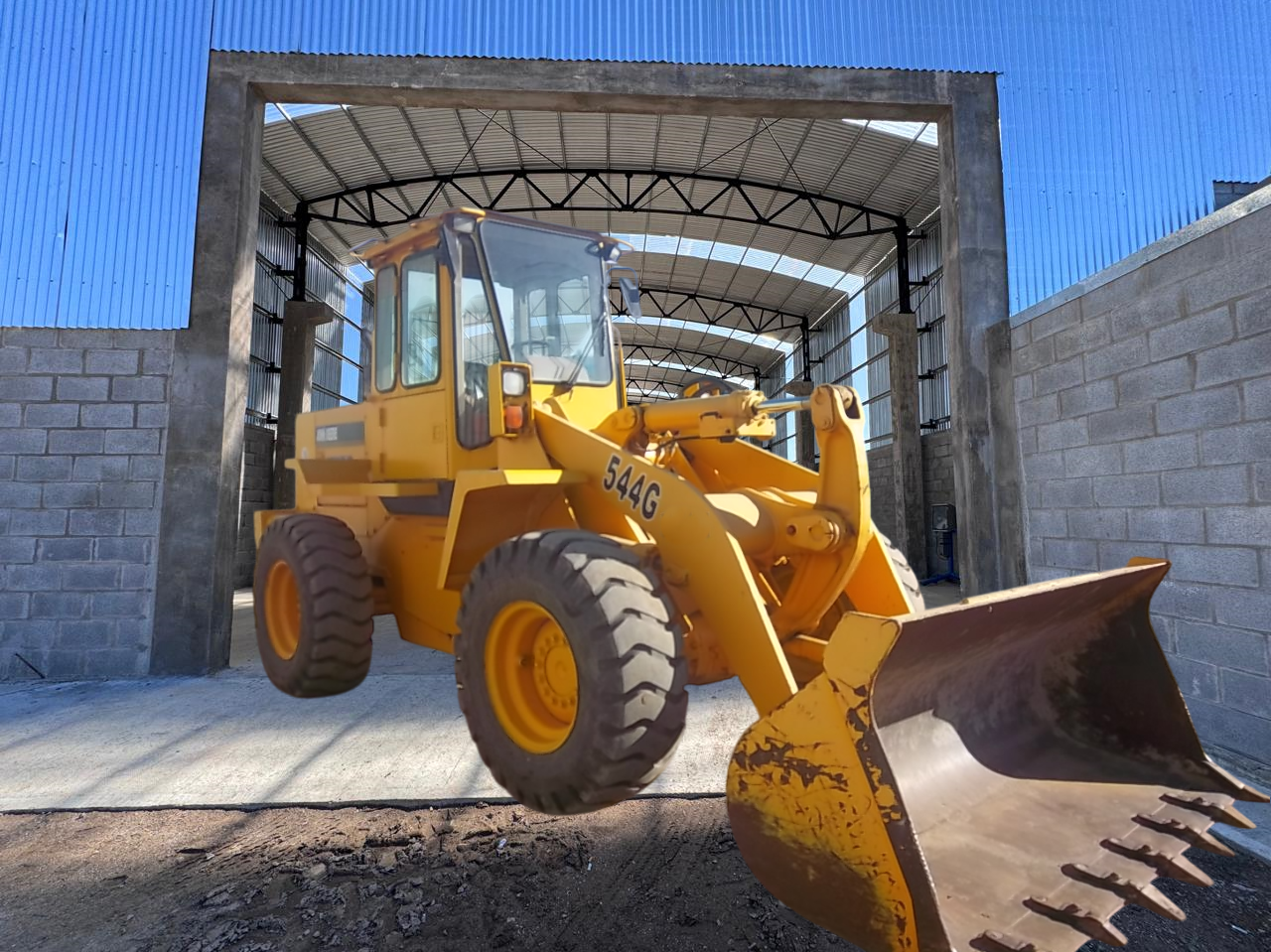 Cargador frontal amarillo estacionado dentro de un refugio de concreto y metal.