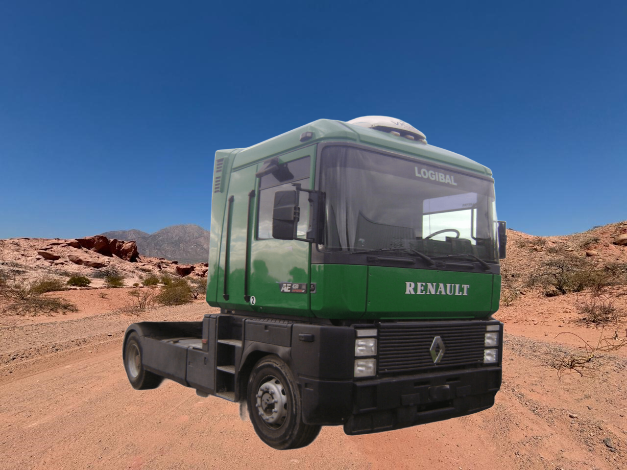 Cabina de camión Renault verde y negra en un camino de tierra en un paisaje desértico.