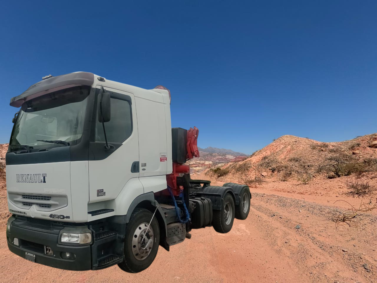 Camión Renault blanco en un camino de tierra en un paisaje desértico con montañas de color marrón rojizo.