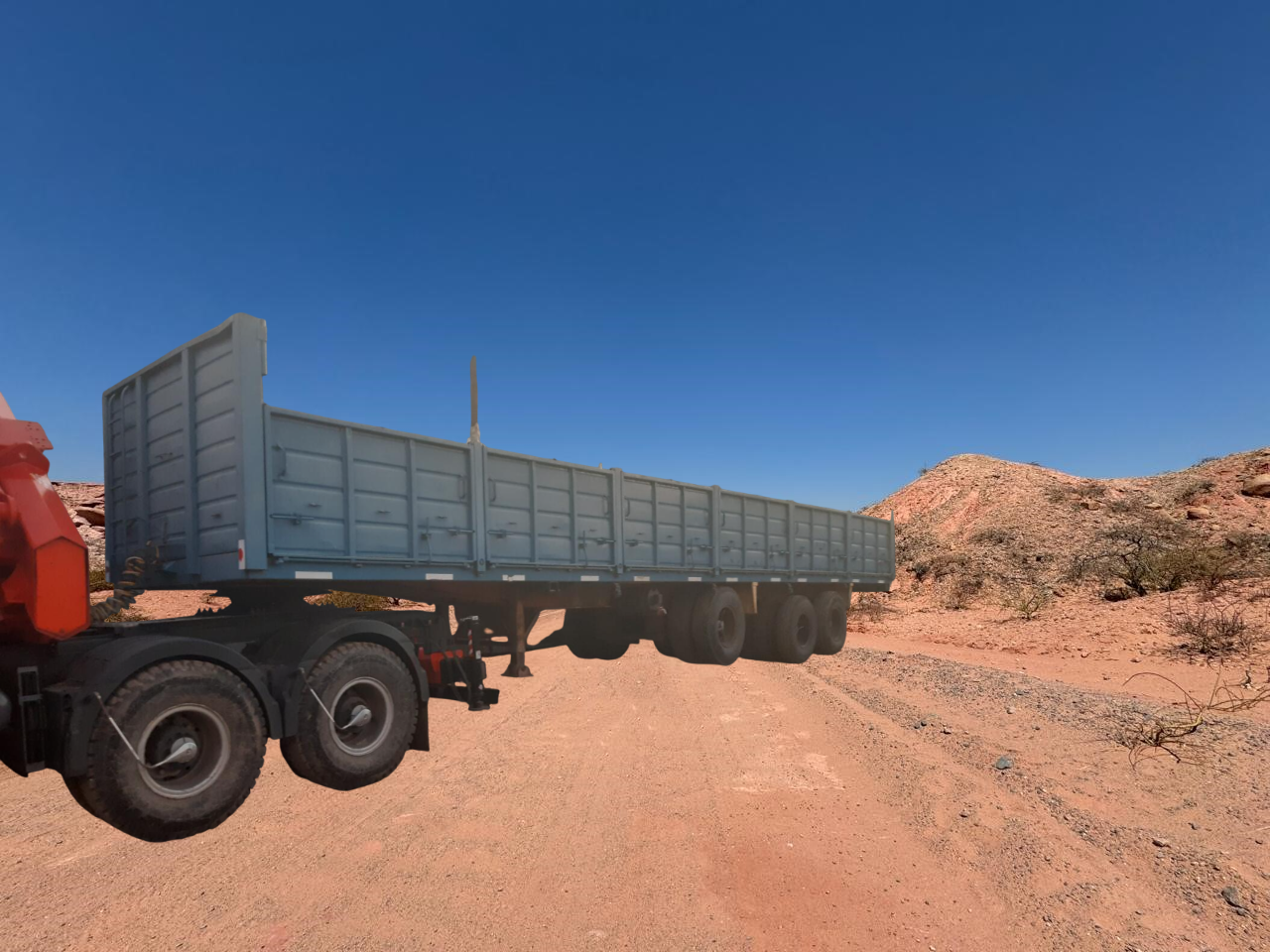 Remolque de camión semirremolque en un camino polvoriento en un paisaje desértico bajo un cielo azul claro.