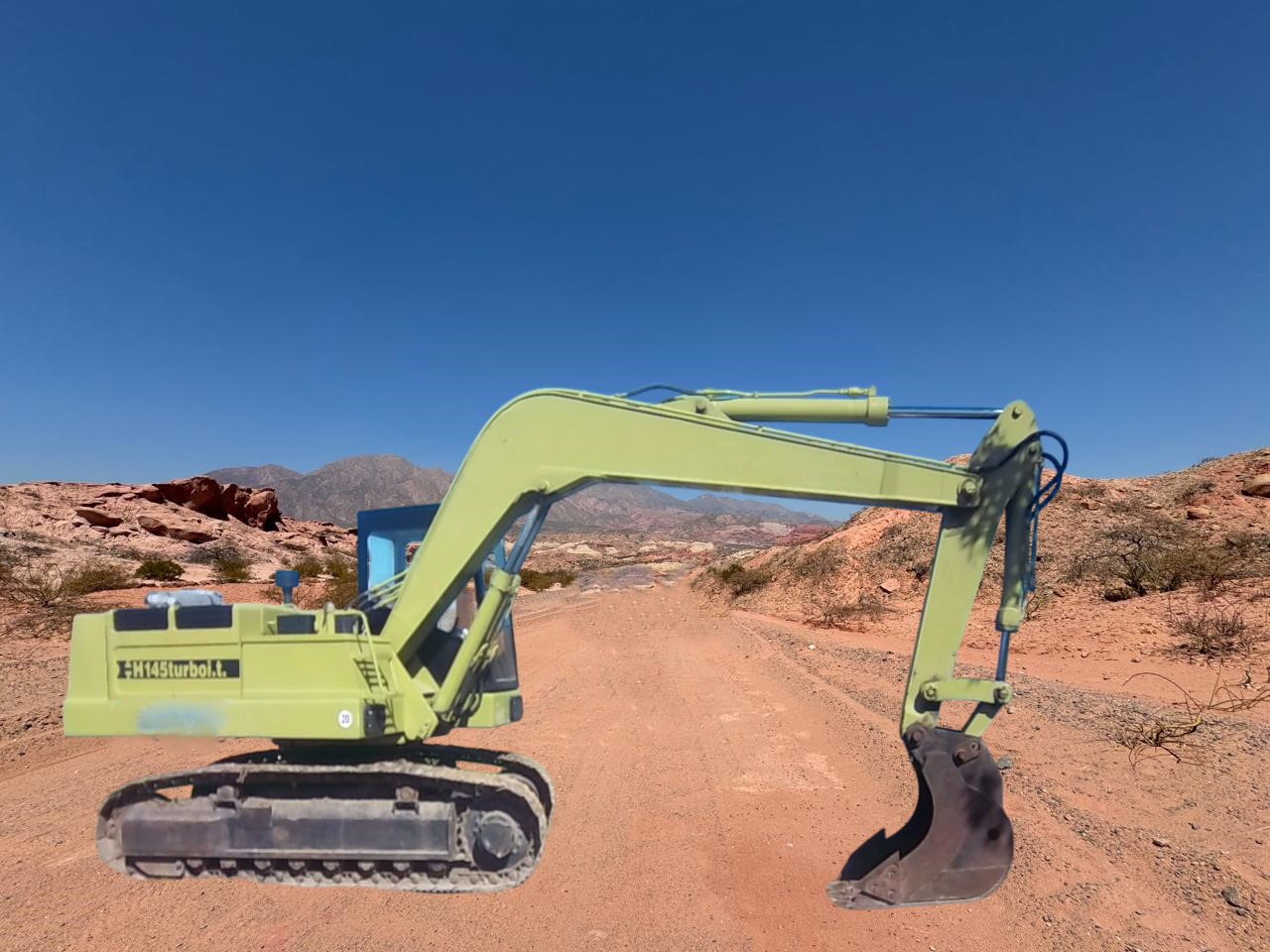 Excavadora verde en un camino de tierra en un paisaje desértico.