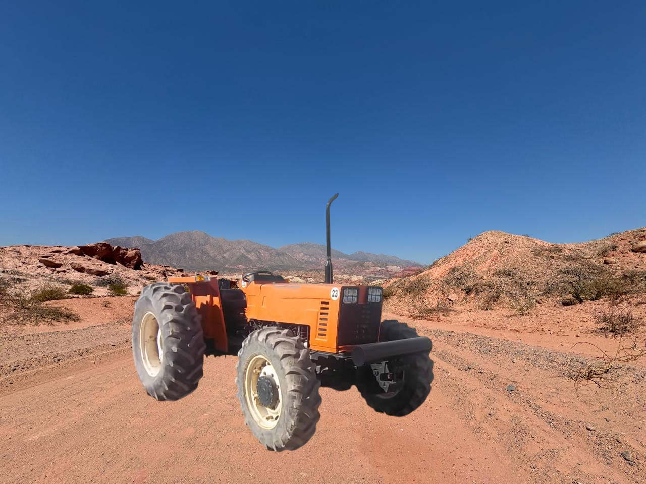 Tractor naranja en un camino de tierra en un paisaje desértico con montañas y un cielo azul claro.