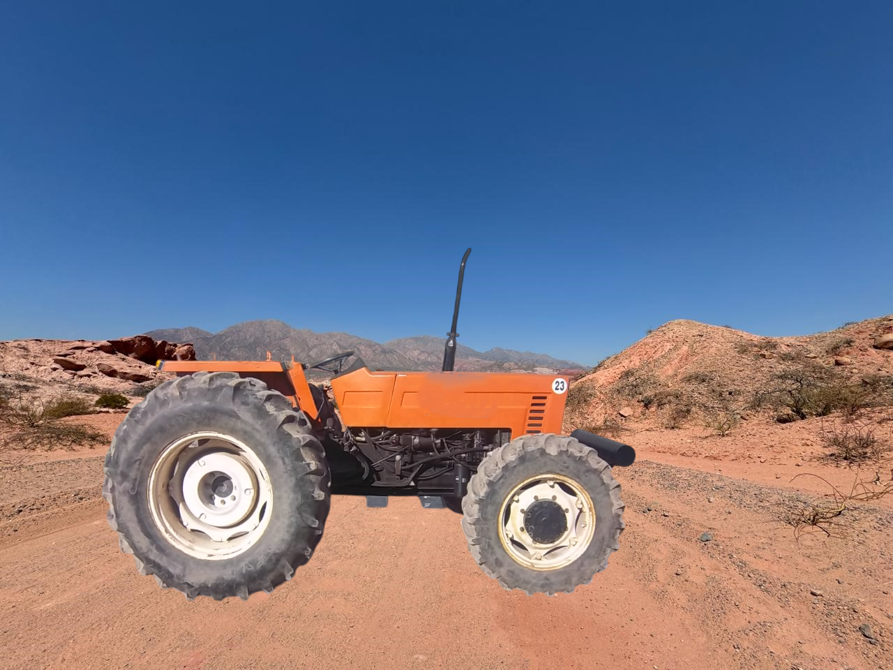 Tractor naranja en un camino de tierra en un paisaje desértico con montañas y un cielo azul claro.