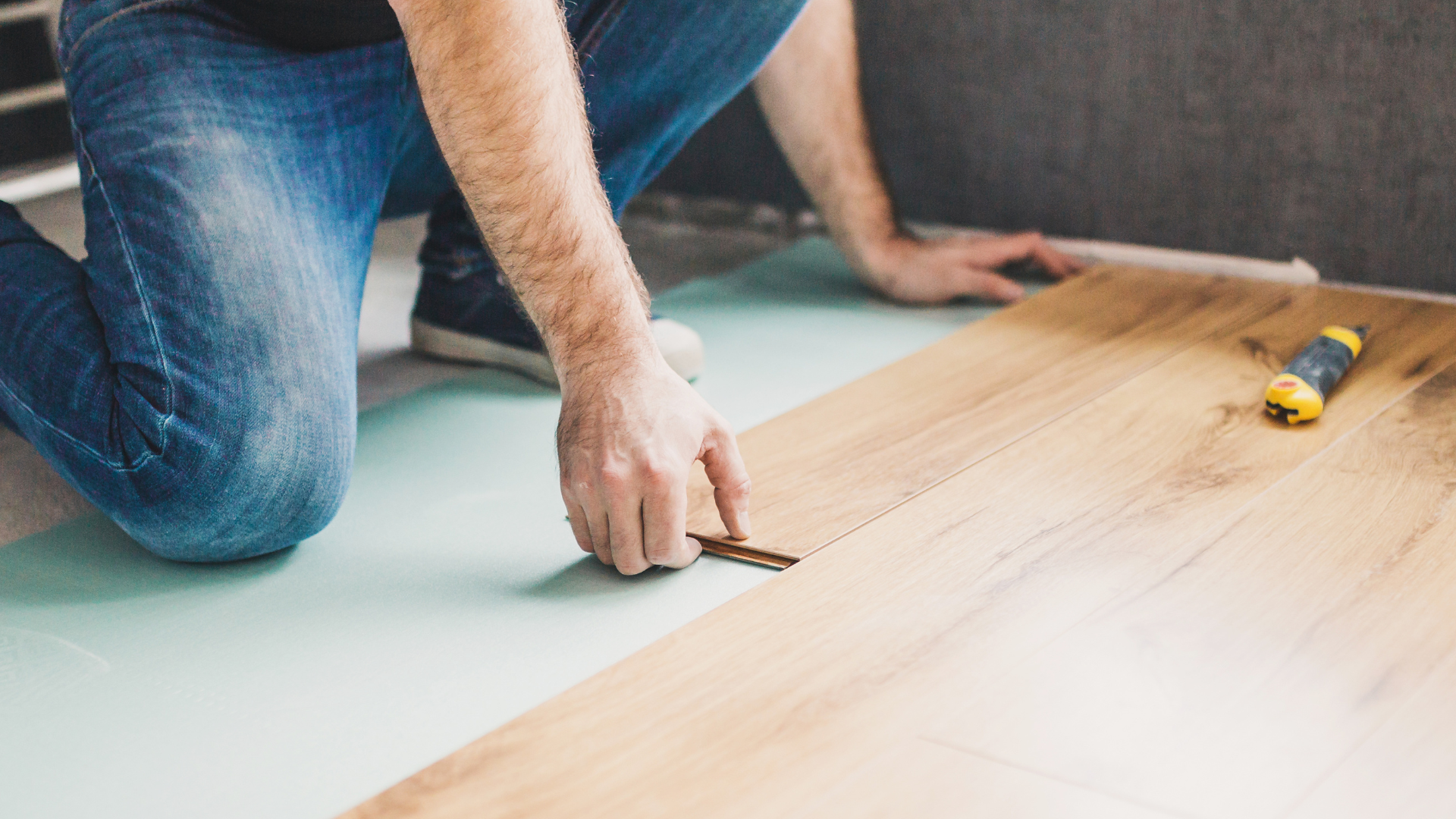 A man is kneeling down to install a wooden floor.