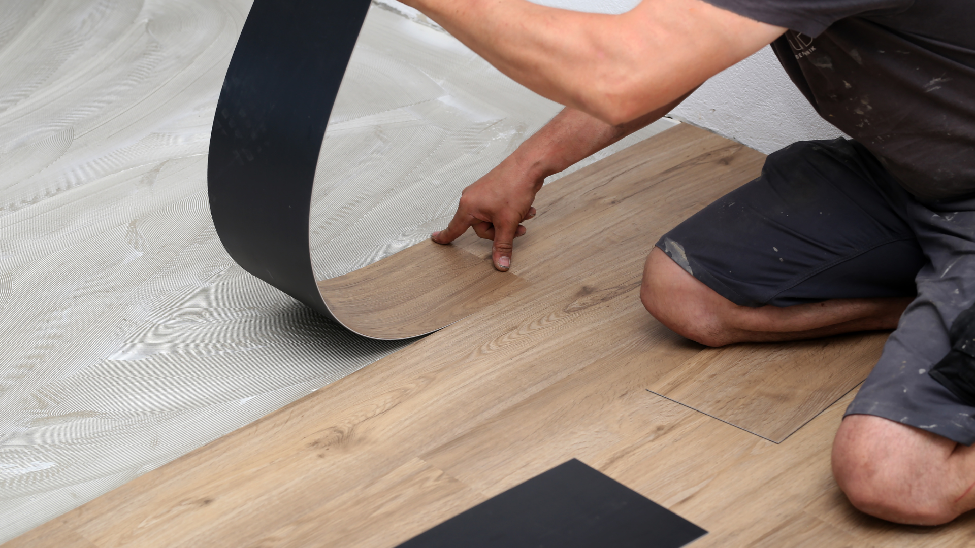 A man is kneeling down while installing a vinyl floor.