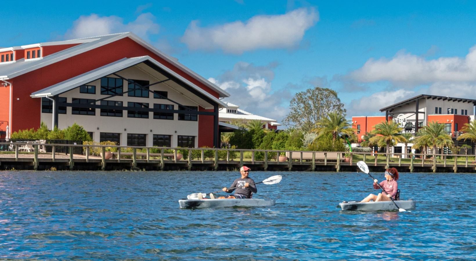 Two people are kayaking on a lake in front of a building.