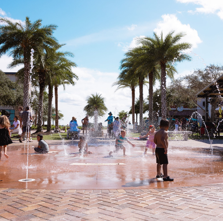 A group of children are playing in a fountain surrounded by palm trees