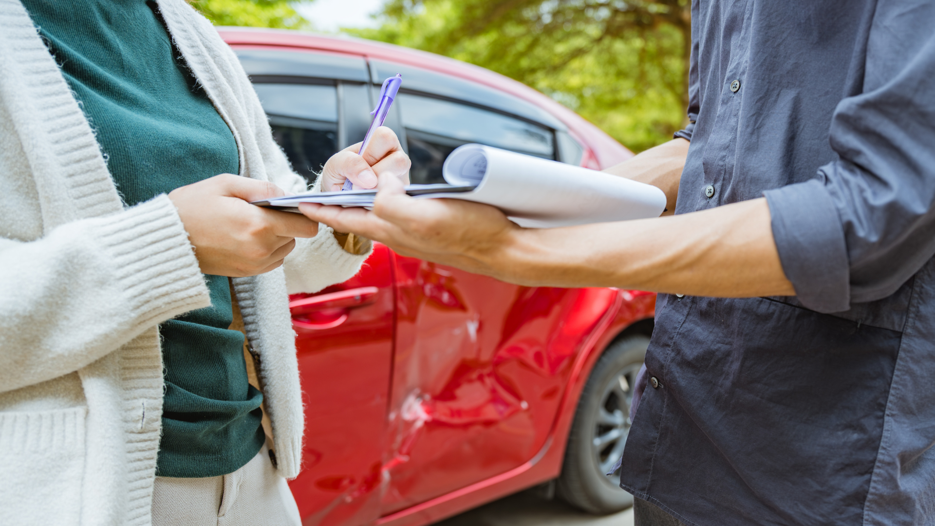 Person handing document and pen to another near damaged red car.
