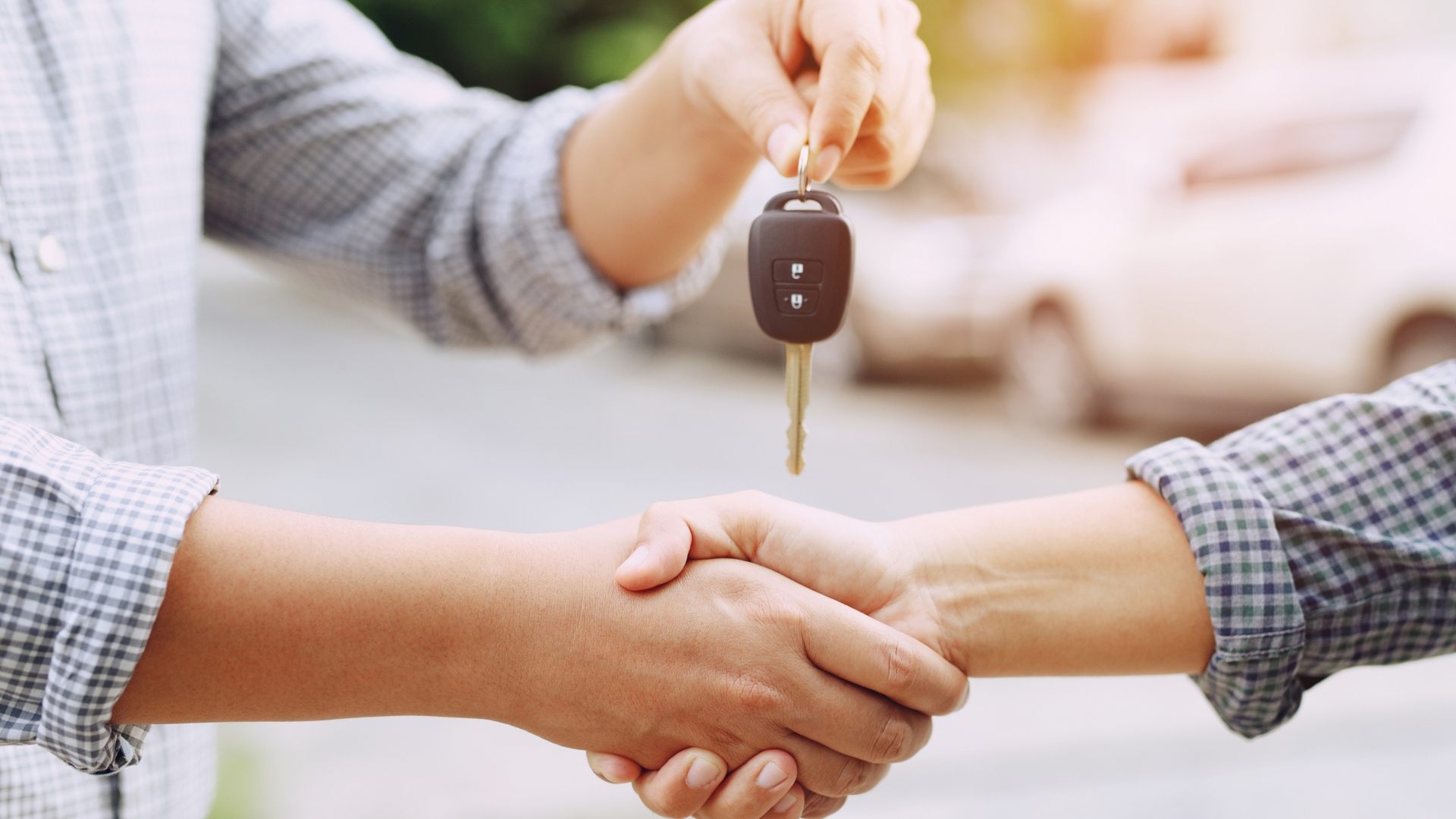 A man is shaking hands with another man while holding a car key.